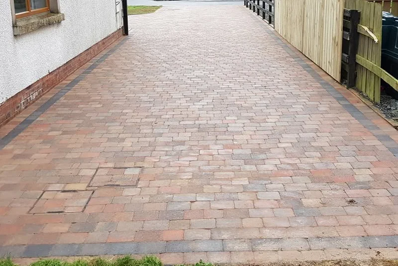 Brick-paved driveway running beside a house and garden boundary